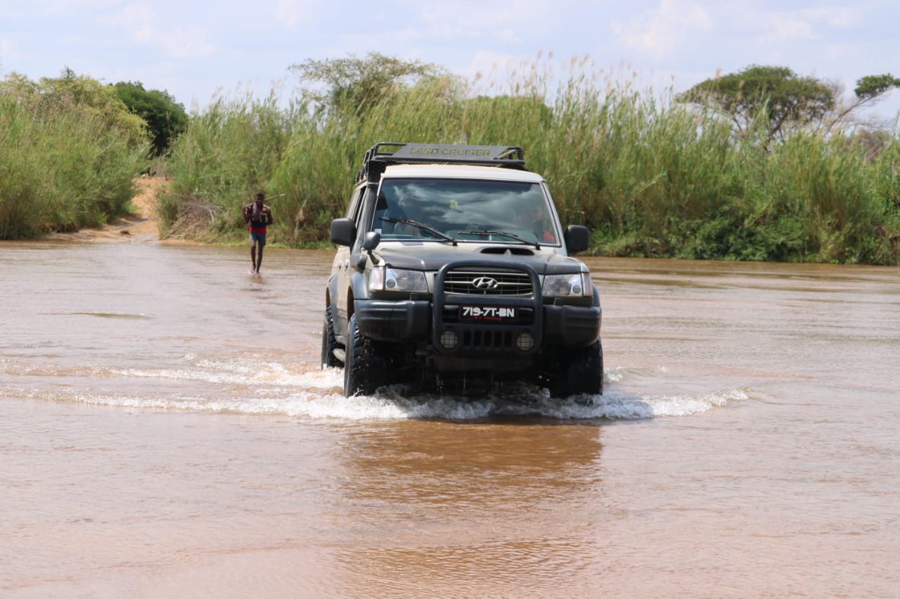 Our 4x4 fording a river in Madagascar, with a man wading across behind it